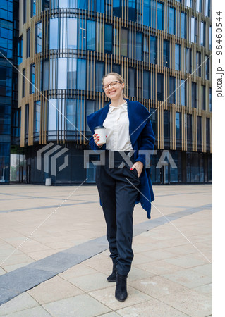 Successful woman in business clothes in blue coat walks down street near office Successful woman in business clothes in blue coat walks down street near office 98460544