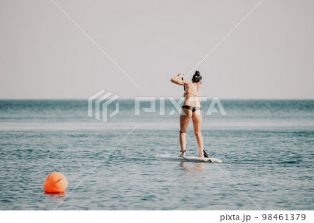 Sea woman sup. Silhouette of happy middle aged tanned woman in rainbow bikini, surfing on SUP board, confident paddling through water surface. Idyllic sunset. Active lifestyle at sea or river. 98461379