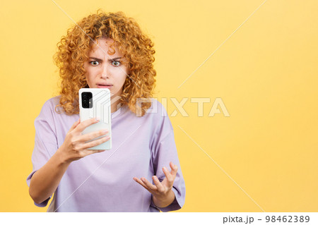 Worried woman with curly hair using a mobile 98462389