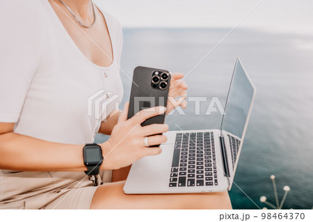 Digital nomad, Business woman working on laptop by the sea. Pretty lady typing on computer by the sea at sunset, makes a business transaction online from a distance. Freelance, remote work on vacation Digital nomad, Business woman working on laptop by the sea. Pretty lady typing on computer by the sea at sunset, makes a business transaction online from a distance. Freelance, remote work on vacation 98464370