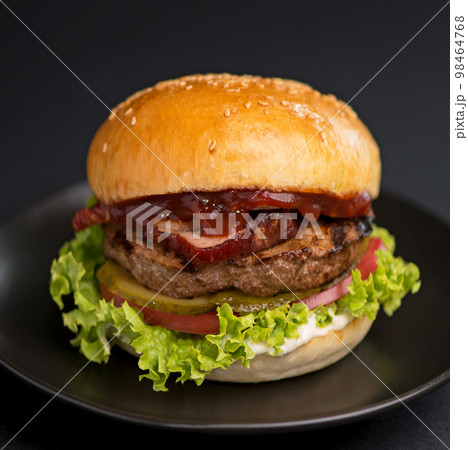 burger with beef patty, lettuce, bacon and pickle on black background 98464768