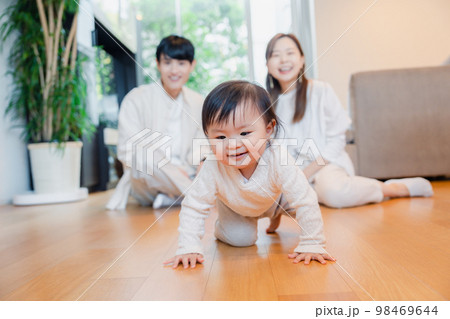 ハイハイをする赤ちゃんと子供の成長を見守る両親 98469644