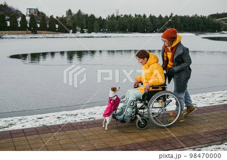 Caucasian woman driving her friend in a wheelchair along the lake in winter. 98470000