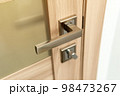 Modern chrome metal door handle on wooden door. 98473267