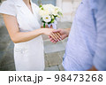 Caressing hands of newlyweds, gentle touch of hands of loving couple. A beautiful and romantic moment holding hands with woman's hand on top of man's hand with wedding gold rings on.  98473268