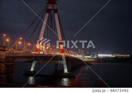 A large automobile bridge on which cars drive at night. A bridge with large columns and lighting. A large automobile bridge on which cars drive at night. A bridge with large columns and lighting. 98473492