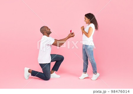 Loving black middle aged man standing on one knee and offering engagement ring to his beloved young woman Loving black middle aged man standing on one knee and offering engagement ring to his beloved young woman 98476014