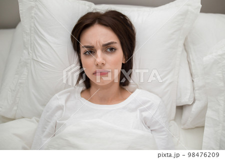 Unhappy young woman lying in bed at home, copy space 98476209