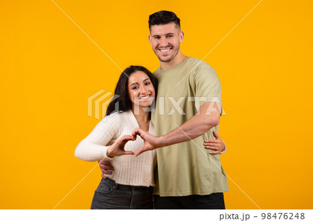 Smiling millennial arabic guy and woman hugging, making heart sign with hands together 98476248