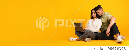 Cheerful millennial arab couple in casual sit on floor, typing in computer, surfing, work and study 98476308