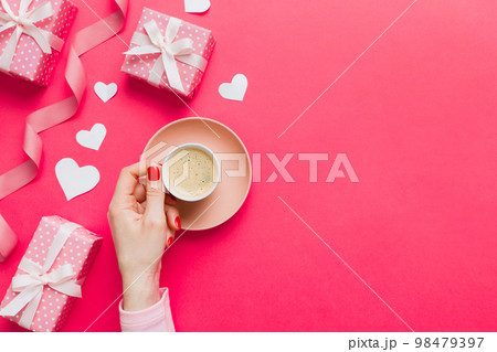 Flat lay of heart shaped cup of black coffee in the hands of women on colored background with copy space top view. Valentine day and holiday concept Flat lay of heart shaped cup of black coffee in the hands of women on colored background with copy space top view. Valentine day and holiday concept 98479397