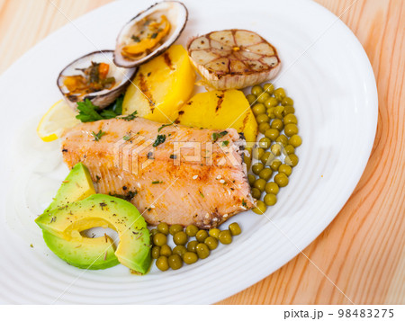 Fried trout fillets served with vegetables, seashells and avocado at plate Fried trout fillets served with vegetables, seashells and avocado at plate 98483275