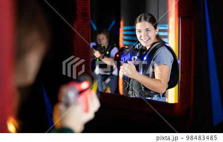 Smiling girl with laser pistol during playing laser tag with her friends in room 98483485