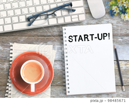 Top view with start up on notebook,keyboard,coffee and glasses on wood table i 98485671