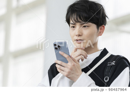 スマートフォン画面を見ながら考え込む若い男性 スマートフォン画面を見ながら考え込む若い男性 98487964
