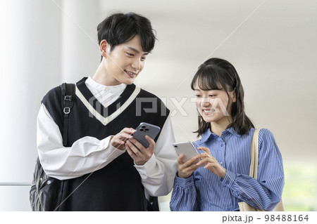お互いのスマートフォンの画面を見る2人の若い男女　 98488164