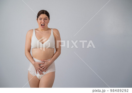 A woman in adult diapers holds her hands on her stomach. Urinary incontinence problem. A woman in adult diapers holds her hands on her stomach. Urinary incontinence problem. 98489292
