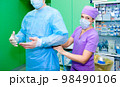 The nurse helps the surgeon to put on his uniform. 98490106