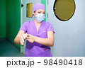 A female surgeon in a mask and surgical uniform disinfects her hands 98490418