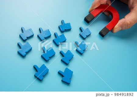 A hand with a magnet attracts social media like symbols. 98491892