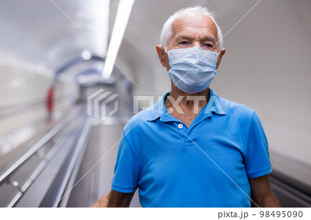 Retired man in protective mask walking down the escalator to metro station Retired man in protective mask walking down the escalator to metro station 98495090