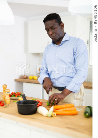 African american man preparing vegetable salad in kitchen African american man preparing vegetable salad in kitchen 98495106