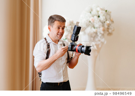 A male photographer in a white shirt with a camera on a leather belt unloading. A male photographer in a white shirt with a camera on a leather belt unloading. 98496549