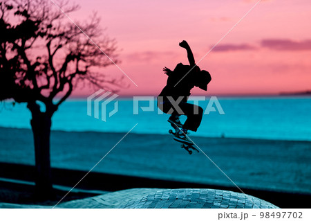 Unrecognizable teenage boy silhouette showing high jump tricks on scooter against Unrecognizable teenage boy silhouette showing high jump tricks on scooter against 98497702