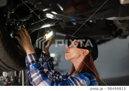 A female mechanic inspects a lifted car. A girl at a man's work. A female mechanic inspects a lifted car. A girl at a man's work. 98499813