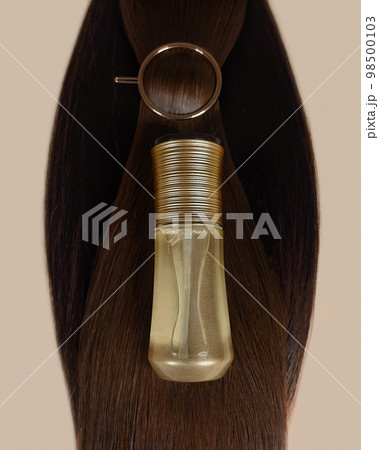A strand of natural dark hair for extensions with a bottle of care product. 98500103