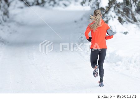 Running in winter, rear view of a female runner on a snowy path in a park or forest Running in winter, rear view of a female runner on a snowy path in a park or forest 98501371