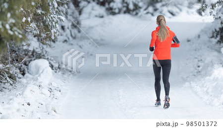 Running in winter, rear view of a female runner on a snowy path in a park or forest Running in winter, rear view of a female runner on a snowy path in a park or forest 98501372