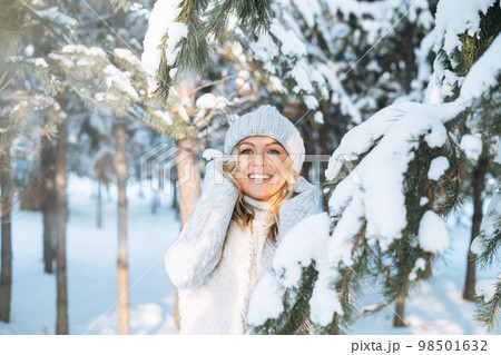 Happy blonde woman in winter clothes hands near face in snowy winter forest 98501632