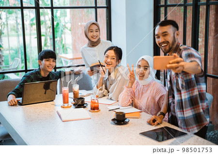 five young asian people smiling taking selfie using cell phone 98501753