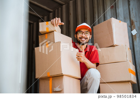 delivery man in red with thumbs squatting between several boxes 98501834