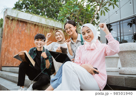 Smiling young people with fists raised while sitting on steps 98501940