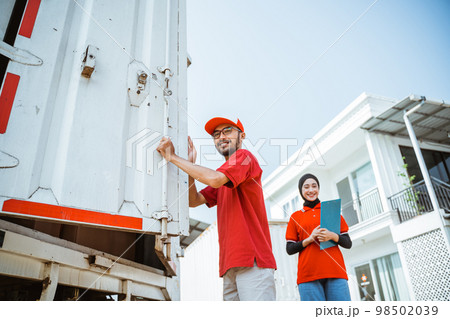 asian delivery worker standing near container against white building background asian delivery worker standing near container against white building background 98502039
