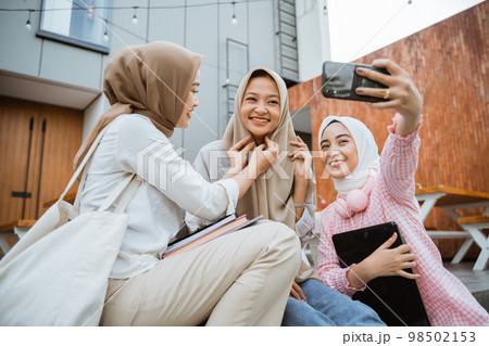 three girls helping wear headscarves during selfie with smartphone 98502153