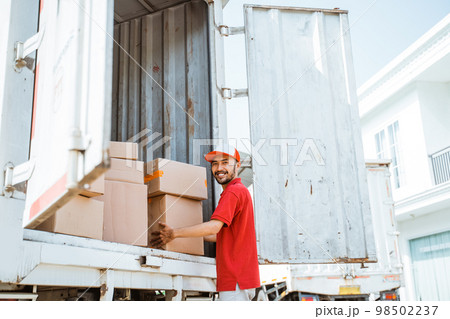 Smiling male employee taking box packages in container while working Smiling male employee taking box packages in container while working 98502237