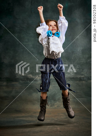 Emotional kid, little girl wearing costume of prince, musketeer and royal person posing over dark vintage style background. Fashion, theater, beauty, emotions concept Emotional kid, little girl wearing costume of prince, musketeer and royal person posing over dark vintage style background. Fashion, theater, beauty, emotions concept 98502508
