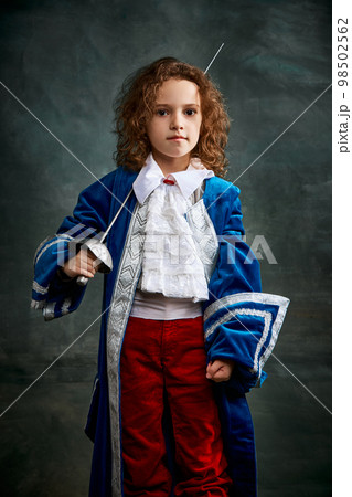 Cinematic portair of beautiful little girl dressed up as medieval knight, little prince over dark vintage style background, Fashion, beauty, emotions, theater concept Cinematic portair of beautiful little girl dressed up as medieval knight, little prince over dark vintage style background, Fashion, beauty, emotions, theater concept 98502562