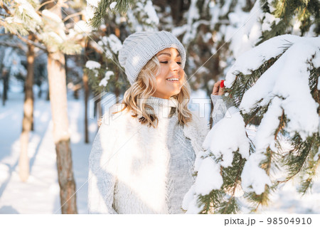 Happy blonde woman in winter clothes hands near face in snowy winter forest Happy blonde woman in winter clothes hands near face in snowy winter forest 98504910