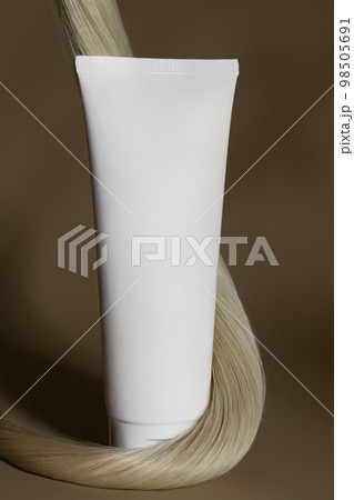 A strand of natural dark hair for extensions with a bottle of care product. 98505691