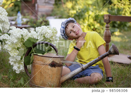 The child is working in the garden. Boy with a vintage watering can and a bouquet of flowers. The child is working in the garden. Boy with a vintage watering can and a bouquet of flowers. 98506306