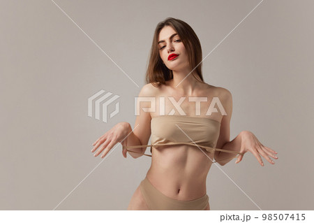Portrait of tender sensual young woman wearing nude color underwear isolated over grey background. Girl with red lipstick. Accent makeup Portrait of tender sensual young woman wearing nude color underwear isolated over grey background. Girl with red lipstick. Accent makeup 98507415