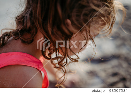 Close-up of little girl during playing on the beach, digging hole in sand. 98507584