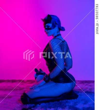 sexy girl in costume and mask bdsm games in neon light with empty background 98507783