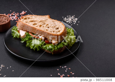 Fresh tasty sandwich with chicken, tomatoes and lettuce on a black plate 98511008