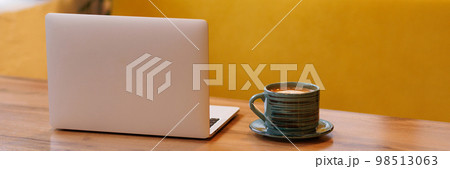 Banner laptop and a cup of coffee on a wooden table in a coffee shop Banner laptop and a cup of coffee on a wooden table in a coffee shop 98513063