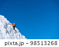 A climber in a red suit climbs an icy white mountain 98513268